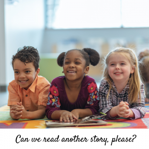 Three smiling children on the floor in front of an open book